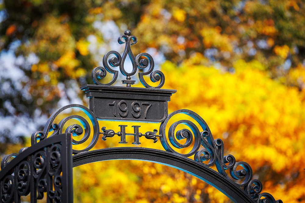 a photo of a Harvard gate with fall foliage behind