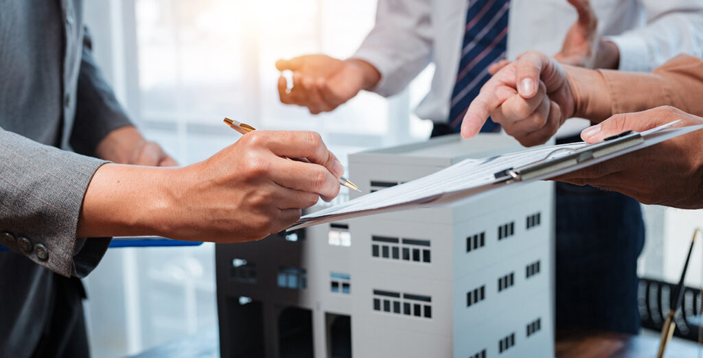 an image of someone signing a contract with a model building in the background