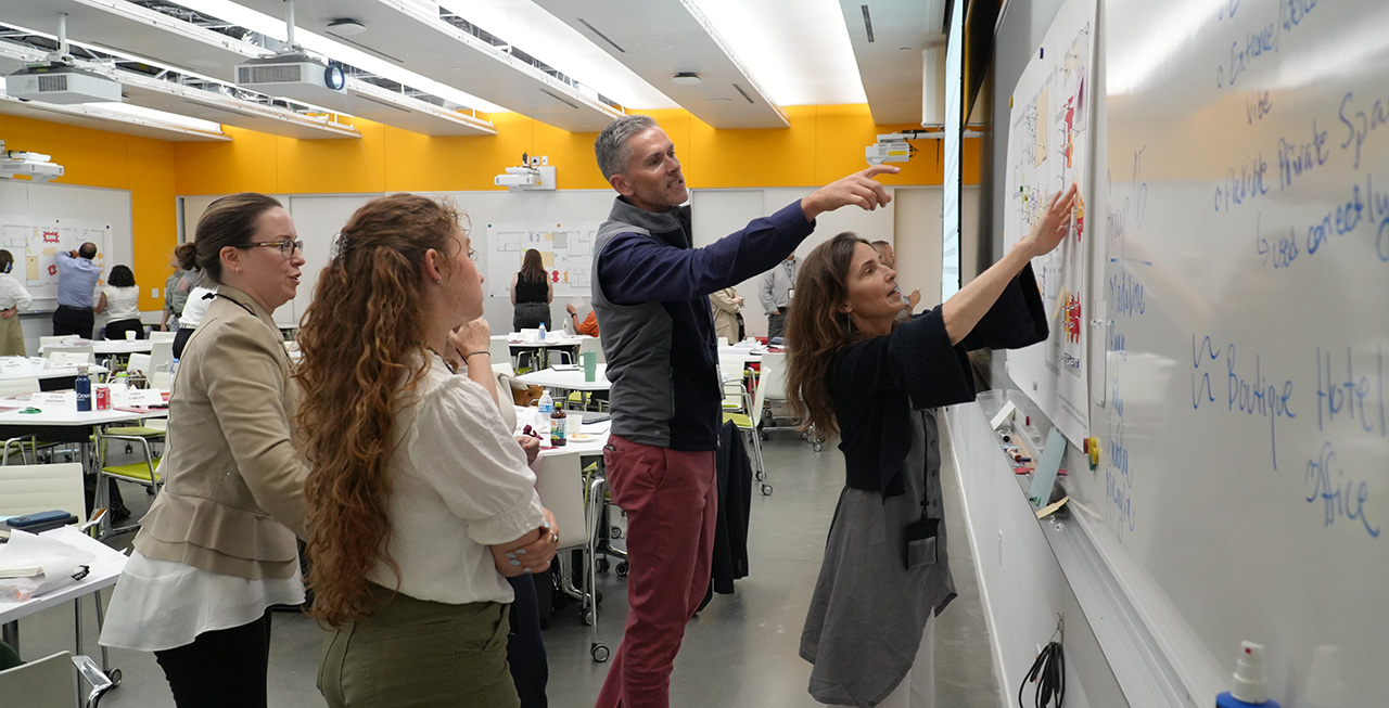 participants in a program pointing at a design on a white board